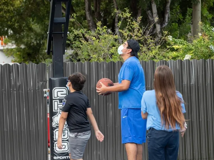 Students play basketball on the center’s outdoor court with a coach.
