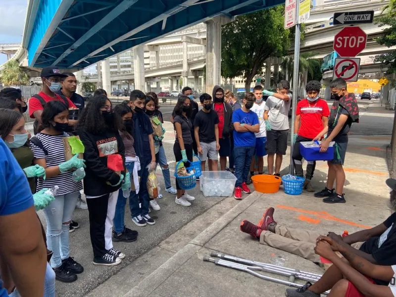 Teens and staff stand with supplies on a sidewalk during a community service outing.