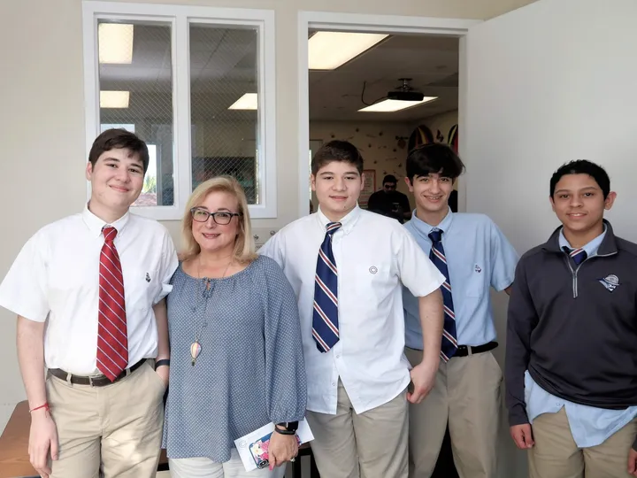 A group of high school students in uniforms stands with a staff member at the center.
