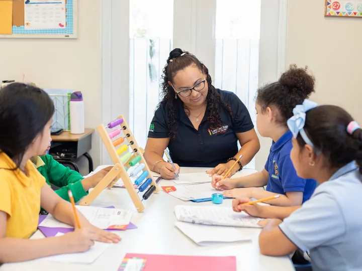 A teacher works through a worksheet with three students at a classroom table.