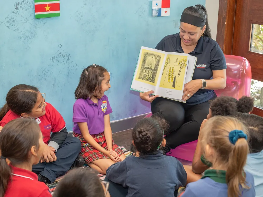 A staff member reads a picture book aloud to a circle of young students.