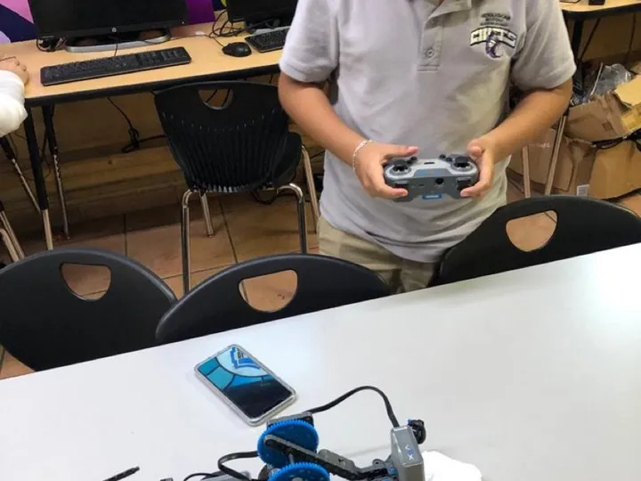 A student controls a small robot built from a robotics kit on a classroom table.