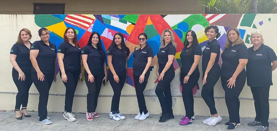 Staff members in matching black polo shirts stand in a row in front of the center’s colorful mural.
