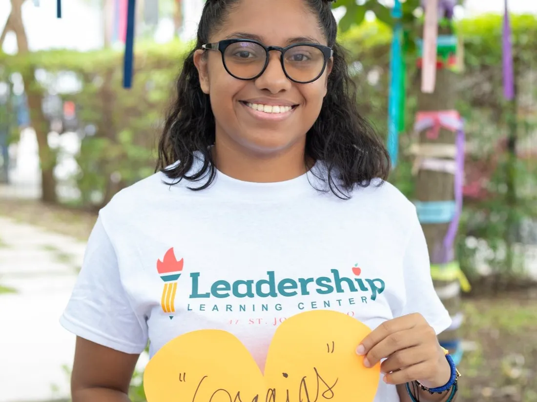 A student in a Leadership Learning Center shirt holds a paper heart that says “Gracias.”