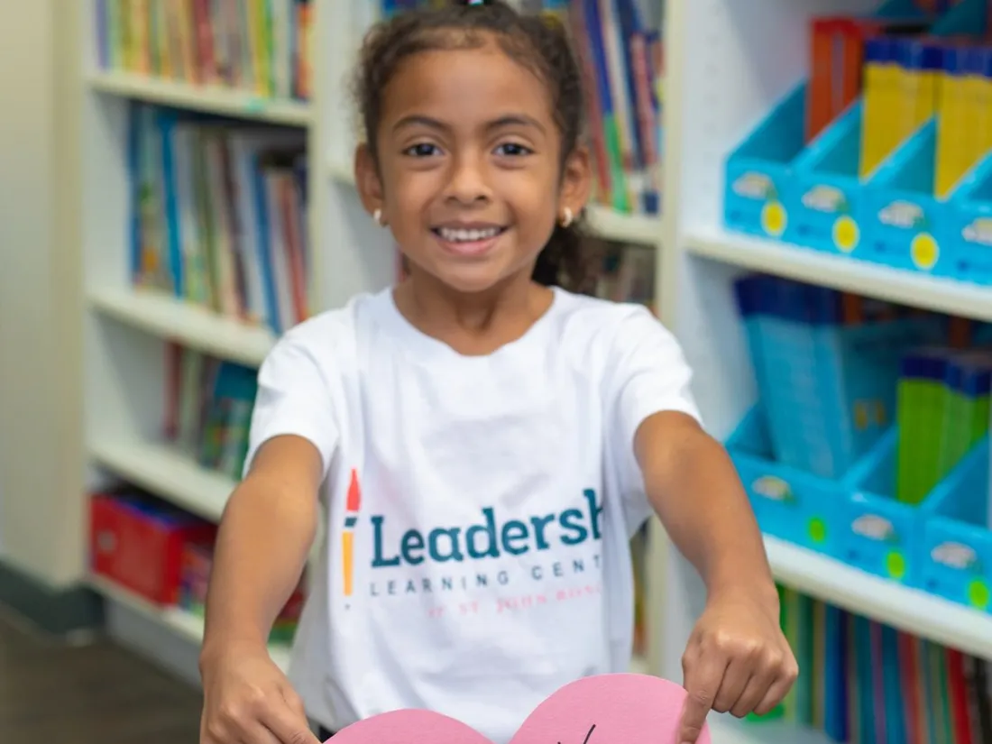 A young student in a Leadership Learning Center shirt holds a paper heart that says “Thank you.”
