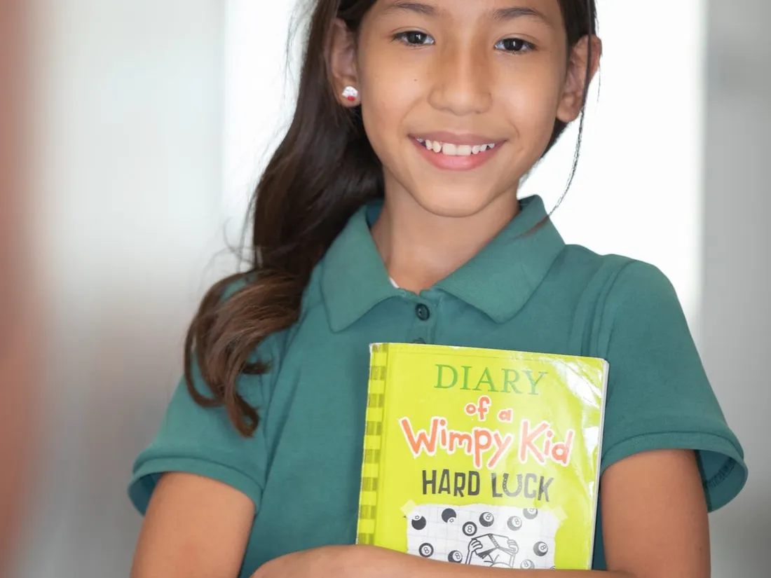 A smiling young student holds a picture book to her chest.