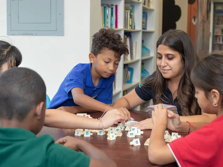 Students and a staff member play a word game together at a table.